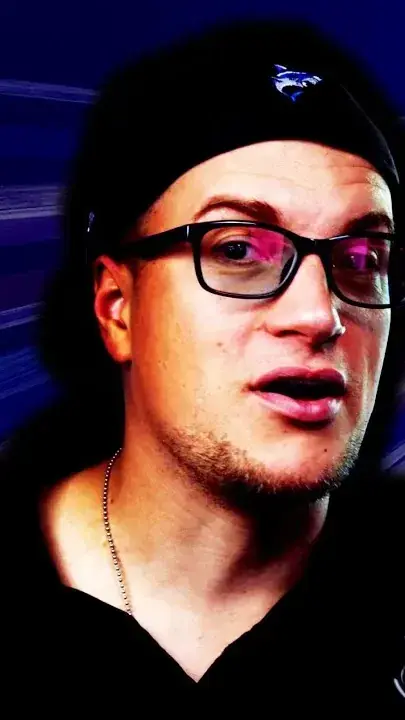Reviewer in a black cap and dark-framed glasses, mid-sentence, against blue streaks